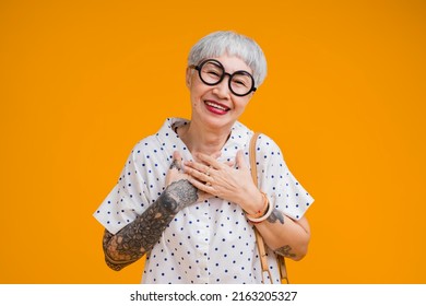 Portrait of attractive funky asian tattoo cheerful grey-haired elder old senior woman touching her chest isolated over yellow pastel background color,surprise and over exited feeling expression