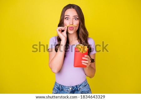 Portrait of attractive funky cheerful wavy-haired girl eating french fries making mustache fooling isolated bright yellow color background