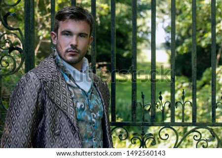 Portrait of attractive gentleman dressed in vintage costume standing in stately home courtyard with railings in background