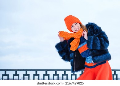 Portrait Attractive Girl Walk In Winter Park On Winter Snow Background. Young Happy Woman In Stylish Warm Outfit And Orange Beanie Hat. Windy Weather