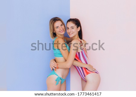 Portrait of attractive girls on the beach Two happy girls posing in swimsuits, smiling and enjoying summer vacation. Summer sea beach. Photo on a blue and pink background