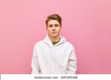 Portrait of attractive guy in casual clothes stands on pink background, looks into camera with serious face, wears white hoodie. Cute young man with blond hair posing, isolated on pink background. - Powered by Shutterstock