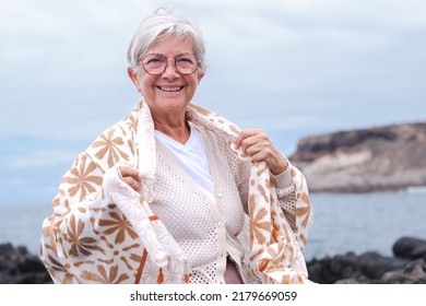 Portrait Of Attractive Happy Senior Woman Sitting On A Pebble Beach Looking At Camera, Elderly Caucasian Female Enjoying Sea, Travel Vacation Retirement