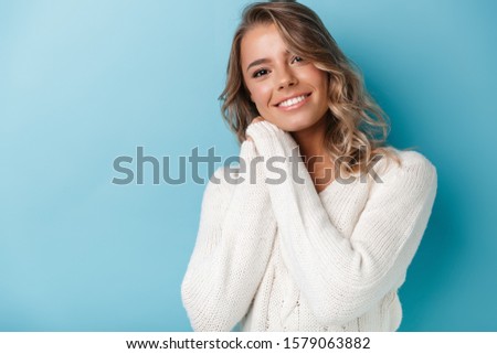 Portrait of attractive happy woman in white sweater smiling and looking at camera isolated over blue background
