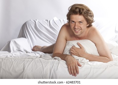 Portrait Of An Attractive Happy Young Man Hiding His Nudity Behind A Pillow. Studio Shot. See More In My Portfolio