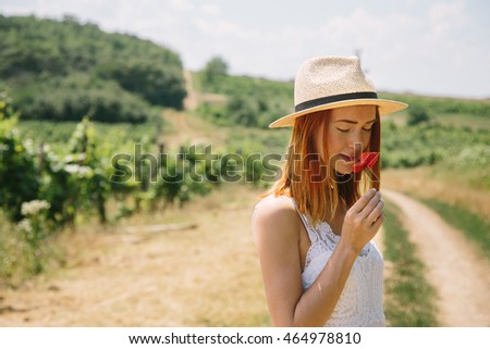 Portrait of attractive hippie young woman wearing boho chic clothes and summer hat outdoors in the golden field smelling red poppy flower. Soft warm vintage color tone. Bohemian fashion style.