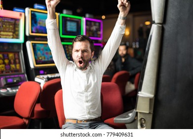 Portrait of an attractive Hispanic man looking very excited about winning some money playing slots in a casino - Shutterstock ID 779409631