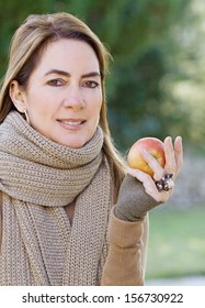 Portrait Of An Attractive Hispanic Middle Aged Mature Woman In A Home Garden Holding A Red Apple Fruit In Her Hand, Looking At Camera With Space, Outdoors.