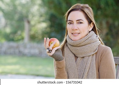 Portrait Of An Attractive Hispanic Middle Aged Mature Woman In A Home Garden Holding A Red Apple Fruit In Her Hand, Looking At Camera With Space, Outdoors.