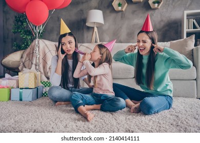 Portrait Of Attractive Irritated Family Sitting On Floor Having Fun Blowing Festal Whistle At Home Indoors