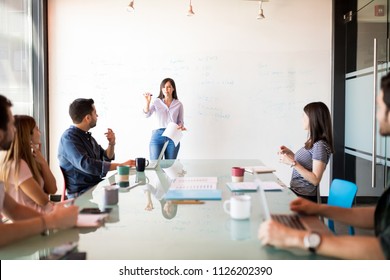 Portrait of a attractive latin woman giving a presentation to coworkers on a white board in a meeting room