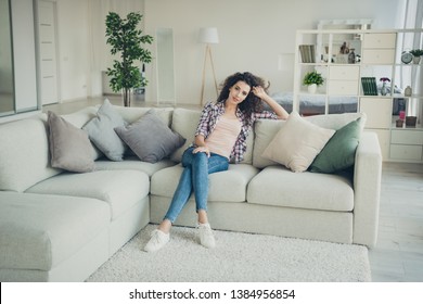 Portrait of attractive luxury millennial house wife have vacation sit divan touch hairdo feel glad dressed denim checked clothing white sneakers in big apartment - Shutterstock ID 1384956854