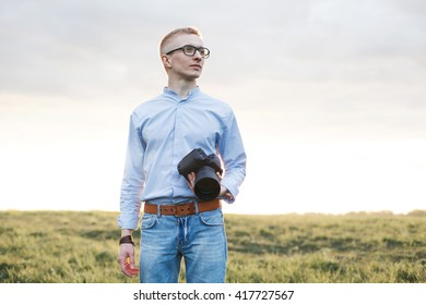 Portrait Of Attractive Male Photographer Outdoors At Sunset. Young Man With A Camera In Hand