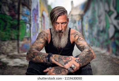 Portrait of an attractive man with a beard and tattoos in a street full of graffiti