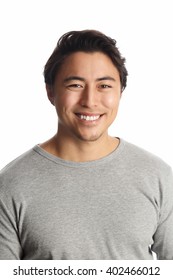 Portrait of an attractive man in his 20s, standing in front of a white background wearing a grey sweater with a big toothy smile.