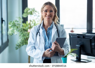 Portrait of attractive mature female doctor looking at camera while holding digital tablet standing in the consultation. - Powered by Shutterstock