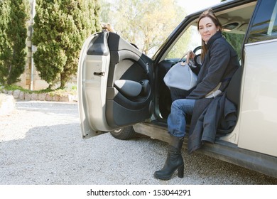 Portrait Of An Attractive Mature Woman Getting Off A Car When Arriving At A Countryside House, Smiling At The Camera During A Sunny Winter Day.