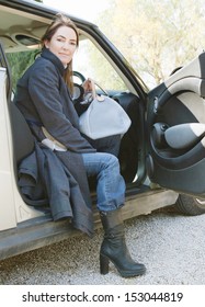 Portrait Of An Attractive Mature Woman Getting Off A Car When Arriving At Her Destination, Smiling At The Camera During A Sunny Winter Day.