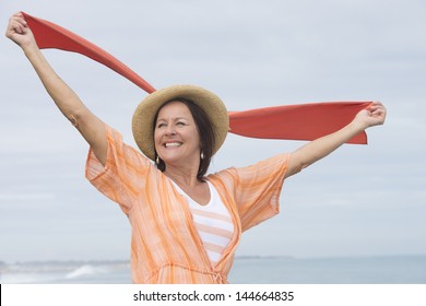 Portrait Attractive Mature Woman Outdoor, Happy And Joyful, Cloth With Arms Up, Smiling, With Ocean And Sky As Blurred Background And Copy Space.