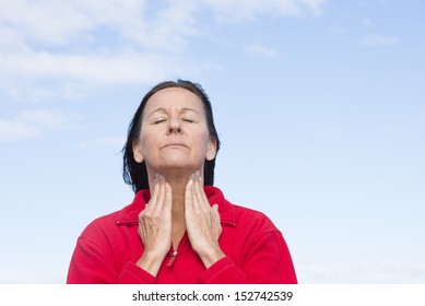 Portrait attractive mature woman stressed and suffering from painful throat ache, closed eyes, concentrated, with hands on throat, blurred sky background and copy space.