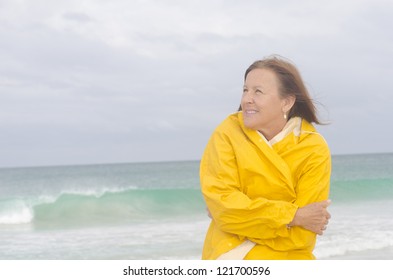 Portrait attractive mature woman with yellow  protective raincoat, isolated with ocean and cloudy autumn sky as blurred background and copy space.