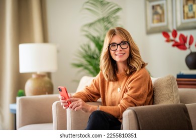 Portrait of attractive mid aged woman sitting in an armchair at home and text messaging. - Powered by Shutterstock