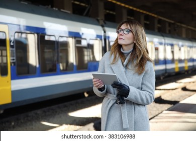 Portrait of attractive middle age businesswoman standing at railway platform at the station and using digital tablet to checking the timetable while waiting for the train.