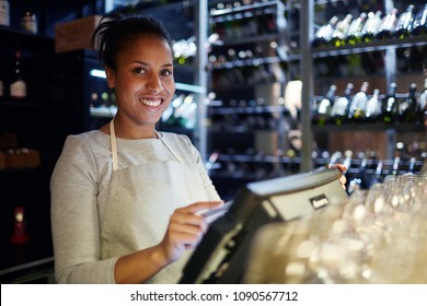 Portrait of attractive mixed race waitress standing at bar counter, using POS system and smiling at camera happily - Shutterstock ID 1090567712