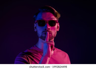 Portrait of attractive mysterious guy showing shh sign keep silence isolated over dark neon violet color background