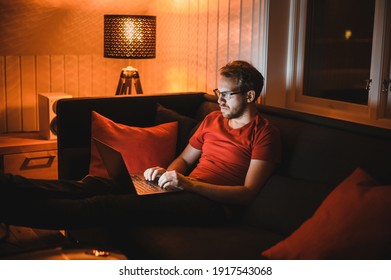 Portrait of attractive nerdy man with glasses is working late night on the computer in living room in home office