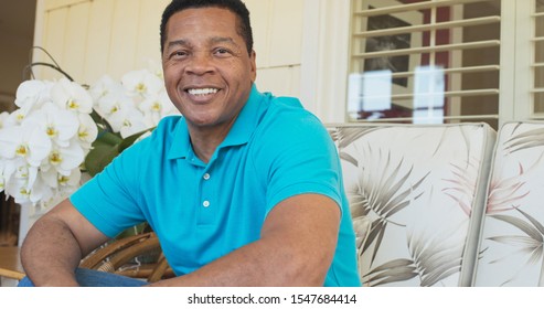 Portrait Of Attractive Older African American Man Smiling While Sitting On Porch Looking At Camera. Happy And Handsome Black Man In His 60s On A Sunny Day