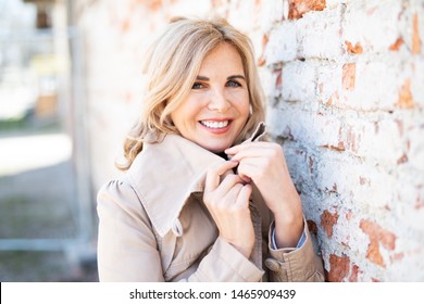 
Portrait Of An Attractive Older Woman With Sympathetic Smile Outside In Trench Coat 