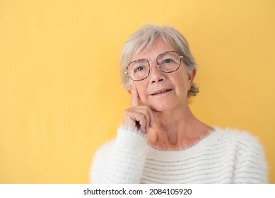 Portrait Of An Attractive Older Woman Wearing Glasses With Thoughtful Expression, Yellow Background