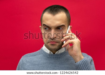 Portrait, attractive, overwrought guy, man talking on phone, looks back to side, front view, bright red background, close up