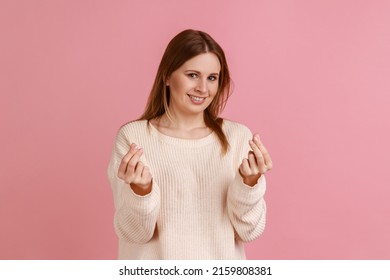 Portrait Of Attractive Positive Blond Woman Smiling And Showing Give Me Money Gesture, Asking For Payment, Allowance, Wearing White Sweater. Indoor Studio Shot Isolated On Pink Background.