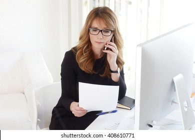 Portrait of attractive professional manager woman making call while analyzing financial data.