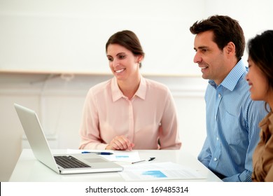 Portrait of attractive professional multi ethnic team looking at laptop while smiling and sitting on office desk
