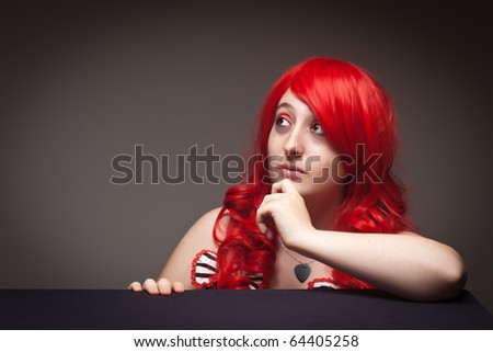 Portrait of an Attractive Red Haired Woman Looking Up with Her Hand on Chin on a Grey Background.