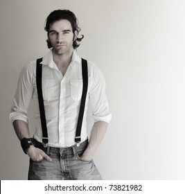 Portrait Of An Attractive Relaxed Male Model In White Shirt, Suspenders, And Jeans With His Hands In Pockets