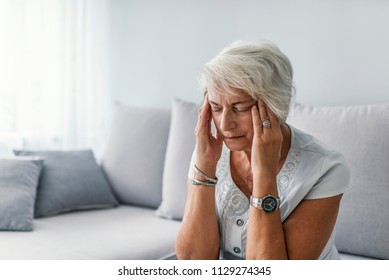 Portrait of an attractive senior woman sitting on a sofa at home with a headache, feeling pain and with an expression of being unwell. - Powered by Shutterstock