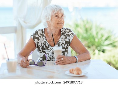 Portrait of attractive senior woman sitting in a summer outdoor cafe and drinking coffee - Powered by Shutterstock