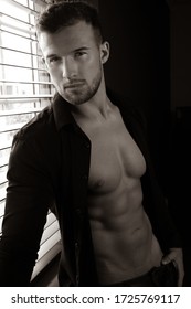 Portrait of attractive shirtless man with stubble standing next to window with with sixpack abs and unbuttoned jeans