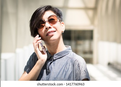 Portrait Of An Attractive Short Hair Asian Woman Wearing 100% UV Light Protect Sun Glasses And Talking On The Phone. Urban Lifestyle, Beauty Middle Aged, Risk Of Eye Damage From UV Light Concept.