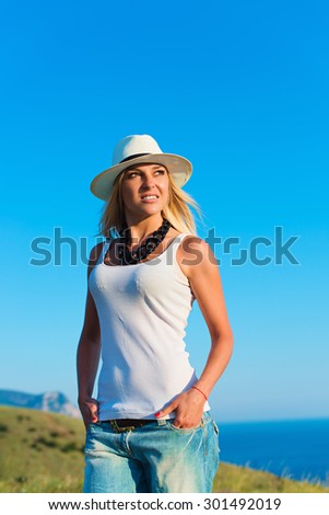 portrait of the attractive, slender, beautiful young Caucasian  blonde girl. Smiling girl enjoys fine warm summer weather highly in mountains against the sea

