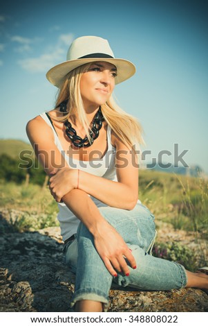 portrait of the attractive, slender, beautiful young Caucasian  blonde girl in a jeans jacket. Smiling girl enjoys fine warm summer weather highly in mountains against the sea