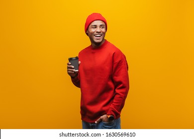 Portrait Of An Attractive Smiling Confident Casual Young African Man Standing Over Yellow Background, Holding Takeaway Coffee Cup