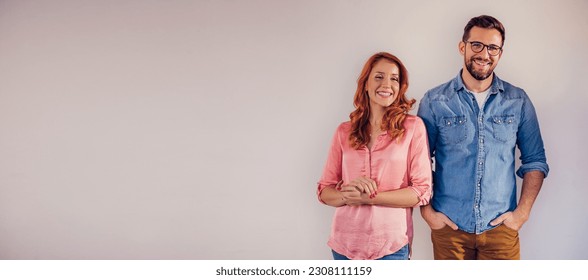 Portrait of an attractive, smiling couple in casual clothes, looking at the camera and standing in front of a gray background. - Powered by Shutterstock