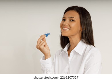 Retrato de una guapa morena sonriente sosteniendo un silbato azul en la mano y mirando a la cámara. Joven feliz con el pelo largo con camisa blanca en un fondo aislado. Ventilador, entrenador, consejero.