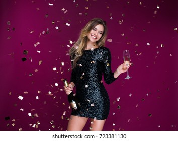 Portrait of attractive smiling girl with tinsel confetti in hands bottle of champange and wineglasses with champagne. New year's feeling. Merry christmas. Happy woman celebrate holiday