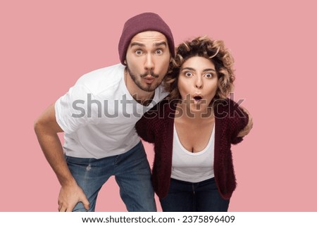 Portrait of attractive surprised shocked couple of friends standing together looking at camera very attentive, expressing shock and astonishment. Indoor studio shot isolated on pink background.